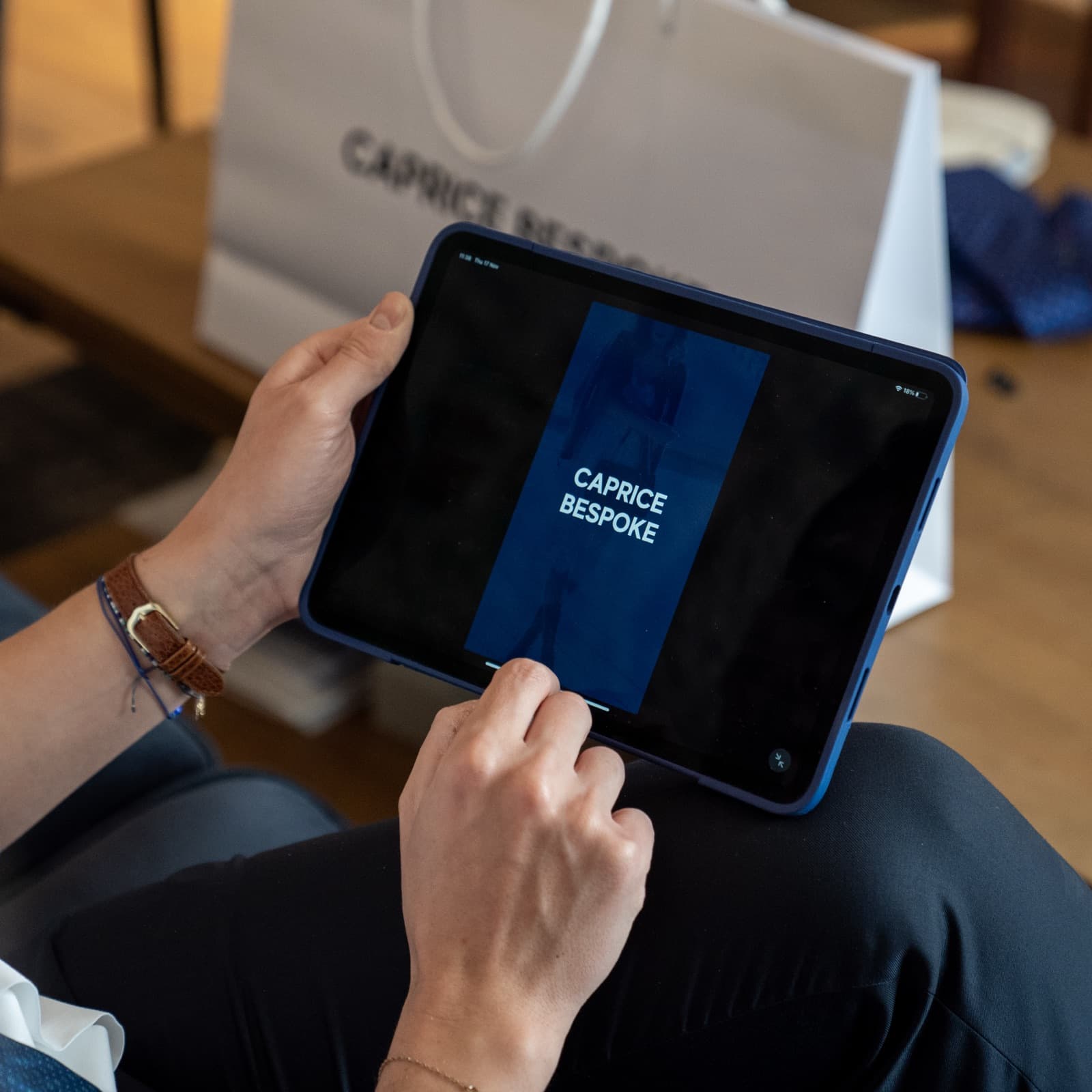 A member browsing the Caprice app on a tablet beside Caprice Bespoke shopping bags