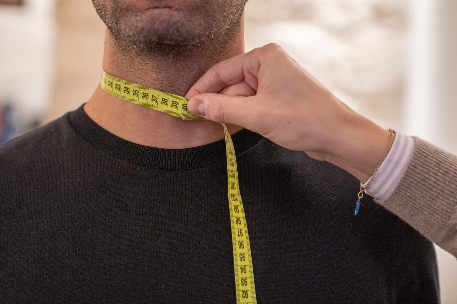 A tailor's tape measure taken around the neck during a Caprice measuring session