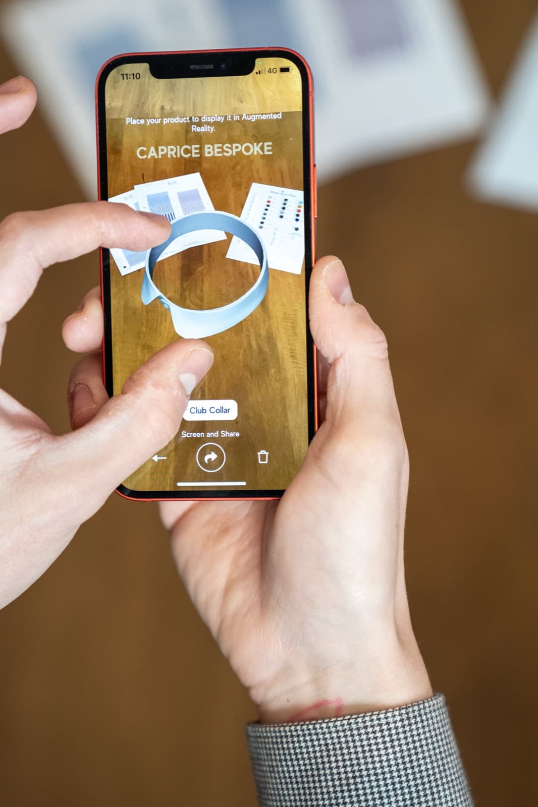 A phone previewing a Caprice garment in augmented reality on a tailoring bench